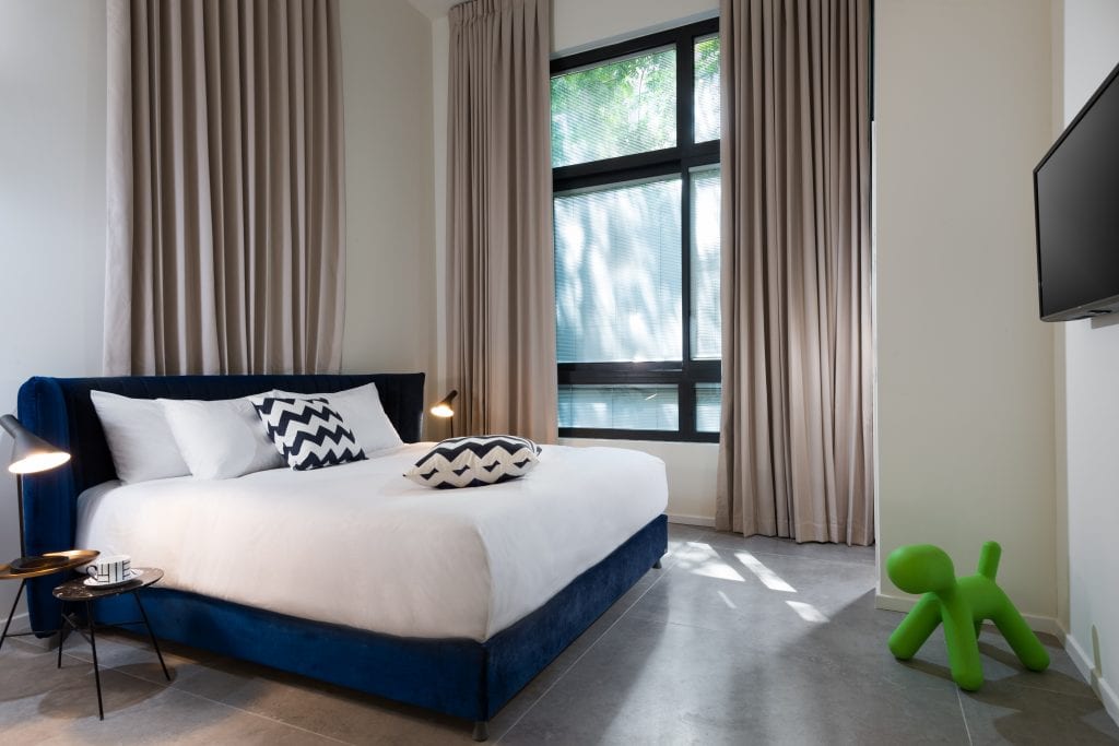 Comfortable bedroom in the Five-Bedroom Duplex Garden at master Shenkin Tel Aviv, featuring a plush bed and a large window that fills the space with natural light.