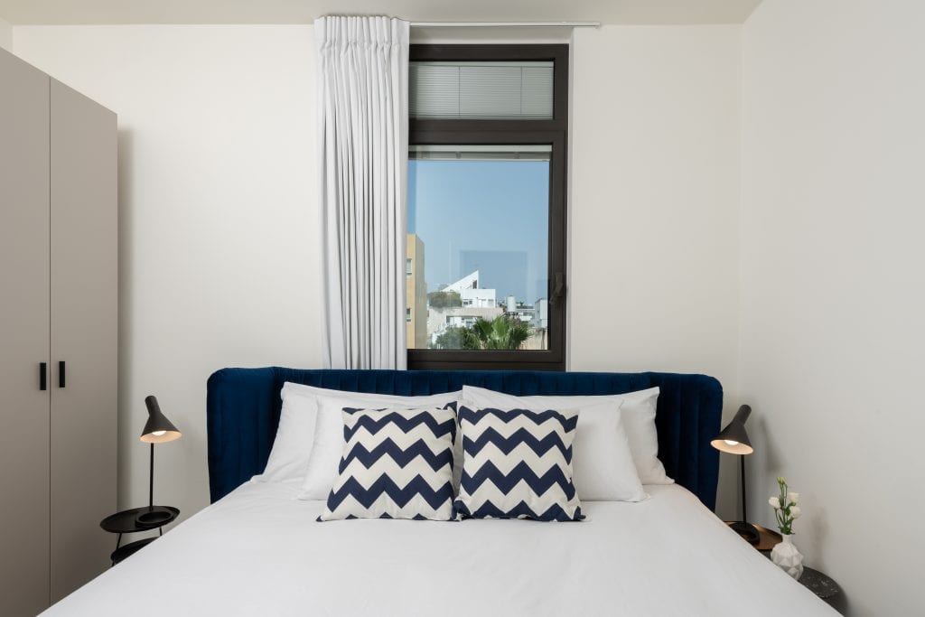 Comfortable bedroom in the Four-Bedroom Apartment at master Shenkin Tel Aviv, featuring a plush bed and a warm, inviting ambiance.