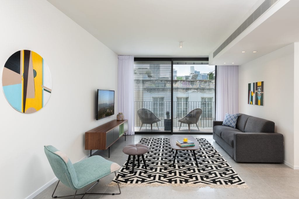 Spacious living area in the Four-Bedroom Apartment with Balcony at master Shenkin Tel Aviv, featuring a glass door leading to a private balcony.