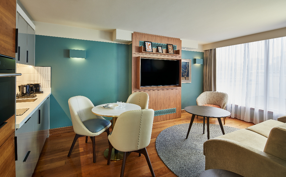 Modern living and dining area at master Farringdon London serviced apartments, with a cozy seating arrangement, round dining table, built-in kitchen, and large windows letting in natural light.