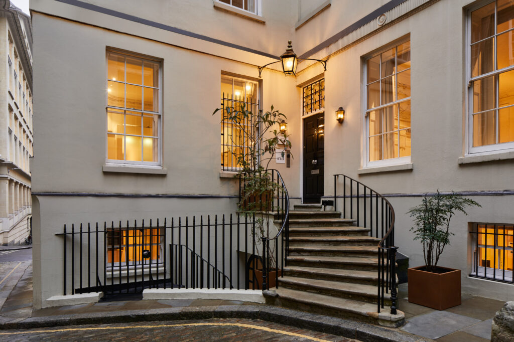 Elegant exterior entrance of master Cannon London apartments featuring warmly lit windows, classic architecture, and a charming curved staircase.