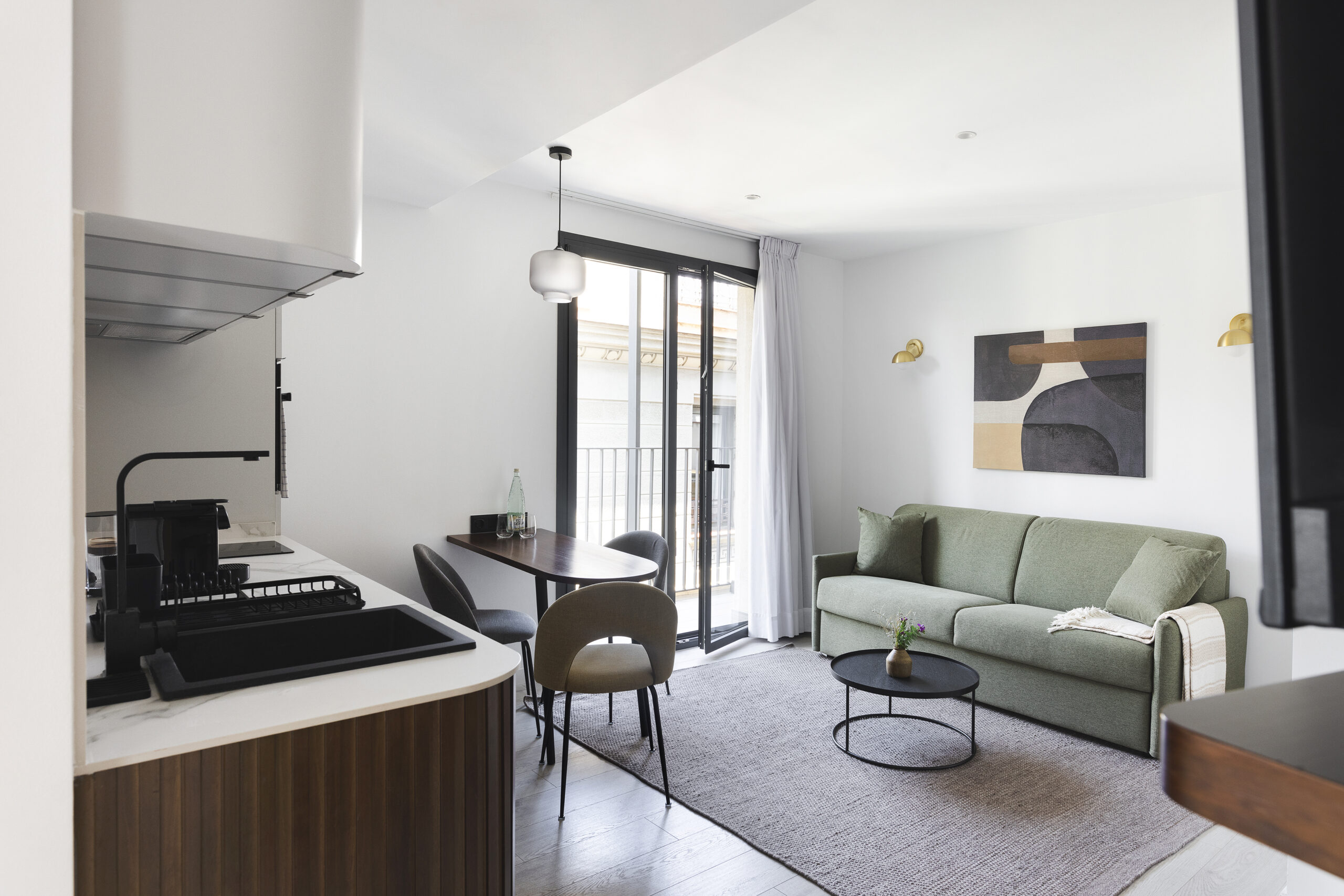 Bright living space at master La Rambla Barcelona with green sofa, round coffee table, dining area, and floor-to-ceiling windows.