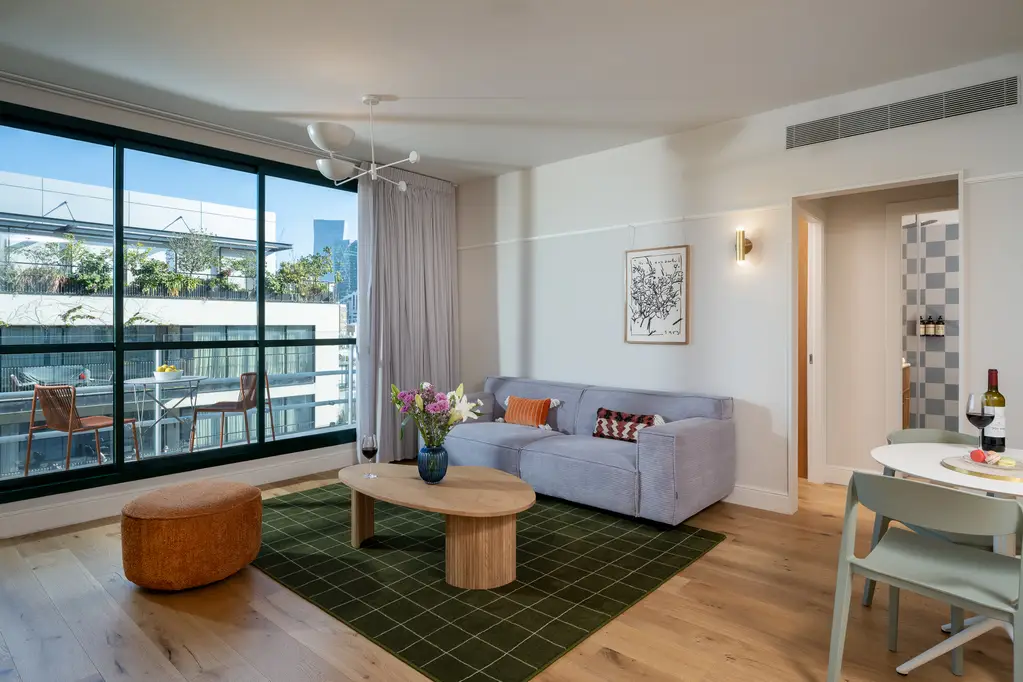 Bright and inviting living area in the One-Bedroom with Balcony at master Mazeh Tel Aviv, featuring a glass door that opens to a private balcony.
